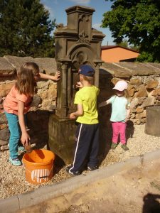 Děti čistí znovu postavený náhrobek v rámci revitalizace zvandalizovaného německého hřbitova při kostele sv. Jana Křtitele ve Vroutku