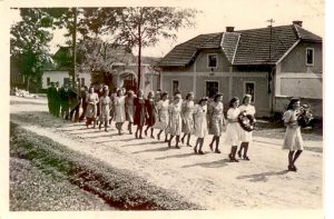 Historický snímek z 50. let 50. století, dívky s věncem následují chlapci.